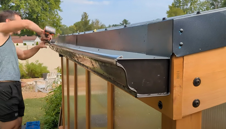 man attaching a gutter to a greenhouse