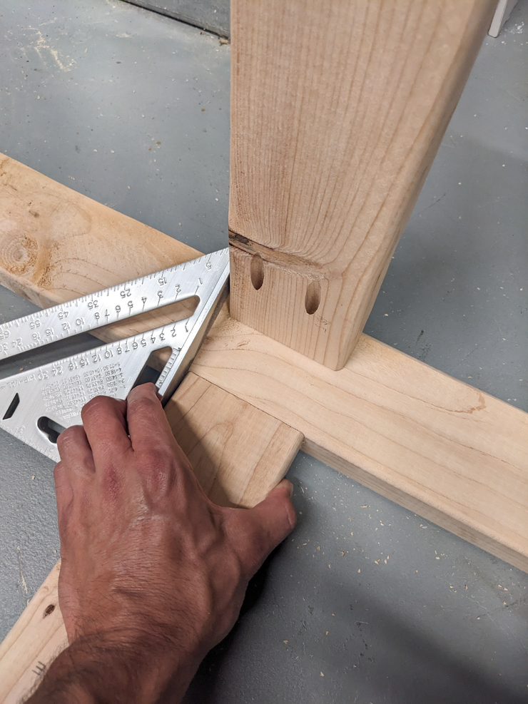 hand holding a speed square and pieces of wood